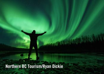 Bright green aurora borealis at night with silhouette of man by river