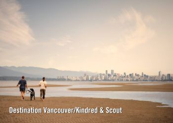 Couple with dog running on Spanish Banks with city in background